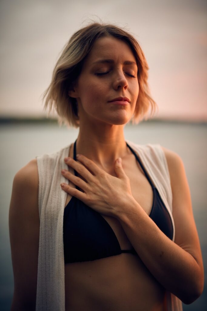 woman in white vest and black bikini with hand on chest connecting with her heart health